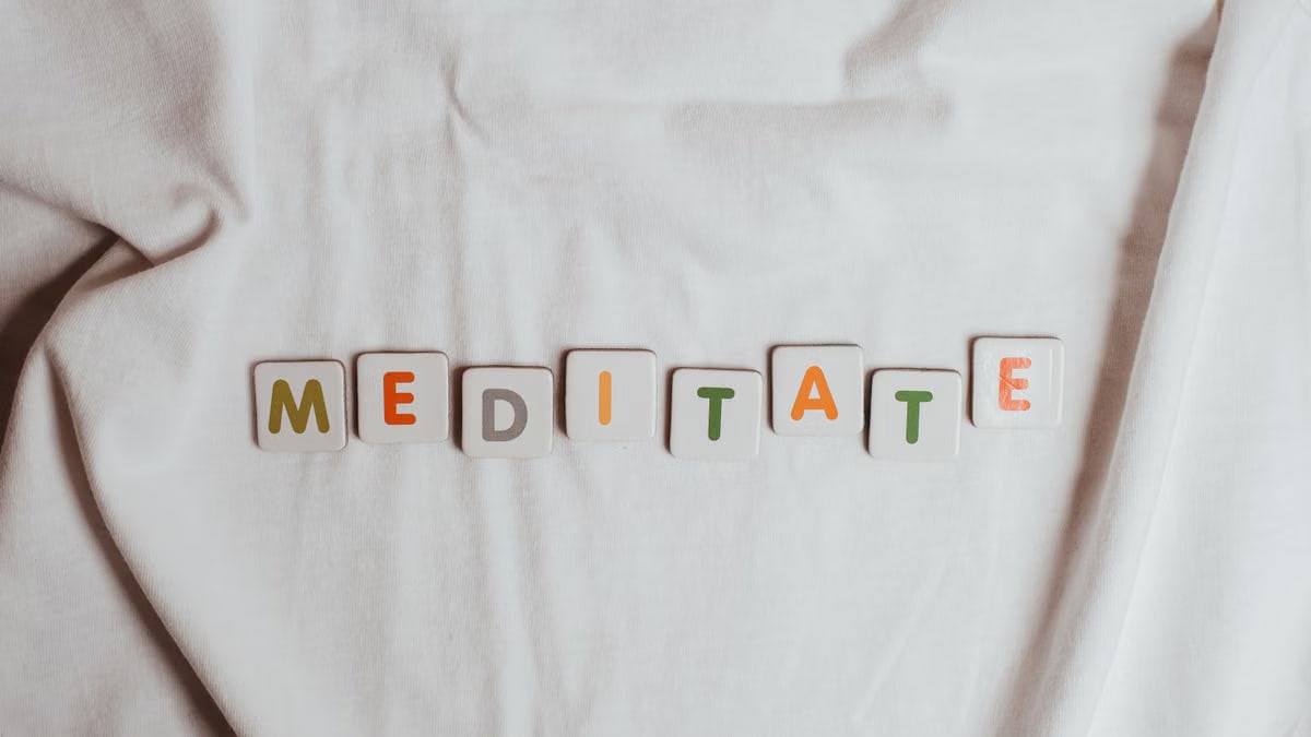 Colorful letter tiles spell 'meditate' on soft white fabric. Perfect for mindfulness themes.